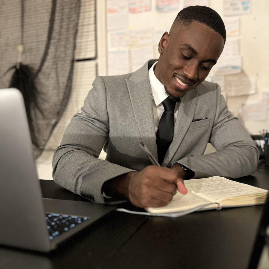 Smiling student doing work on a desk with a laptop, writing notes, for the Advanced Paralegal Apprenticeship.